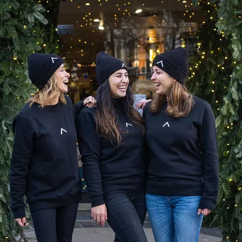 Three smiling people wearing black beanies and sweatshirts embroidered with a white logo