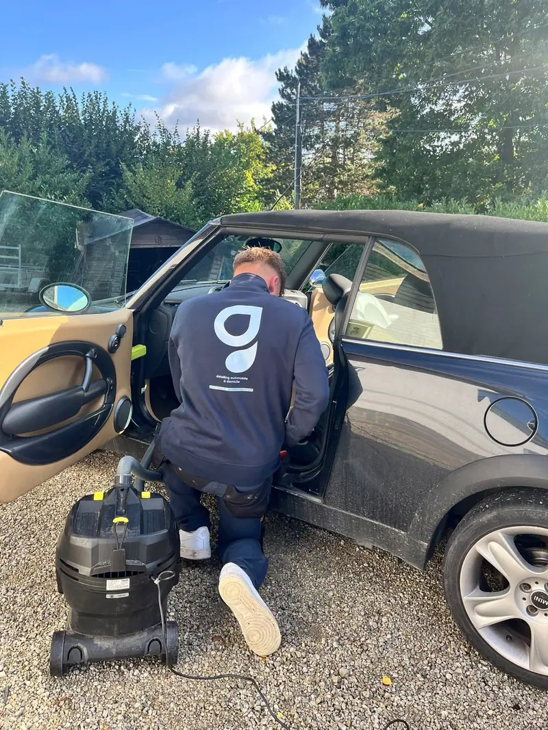 GWash employee in a custom navy sweatshirt foam-washing a car