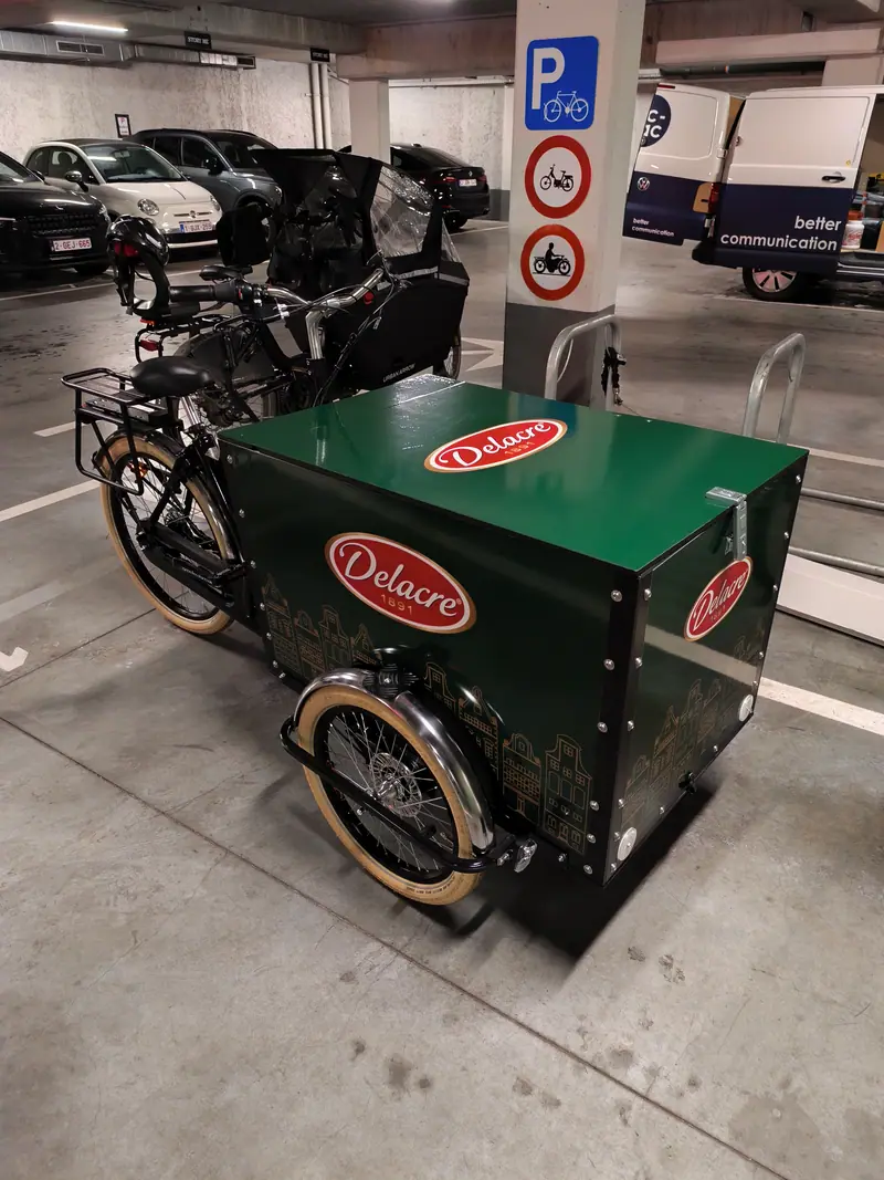 Green cargo bike wrapped with the Delacre logo in a car park