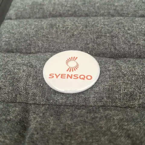 Syensqo badge on grey fabric